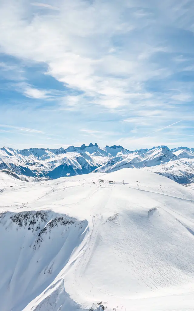 Paysage de montagnes enneigées avec des glaciers et des sommets sous un ciel bleu partiellement nuageux