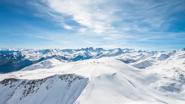 Paysage de montagnes enneigées avec des glaciers et des sommets sous un ciel bleu partiellement nuageux