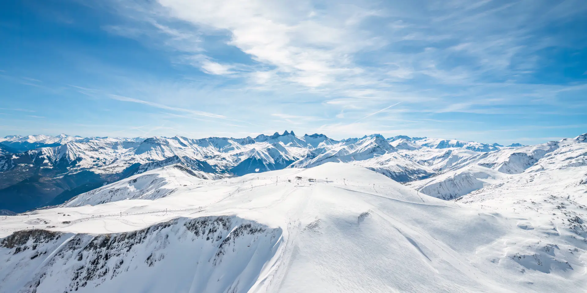 Paysage de montagnes enneigées avec des glaciers et des sommets sous un ciel bleu partiellement nuageux