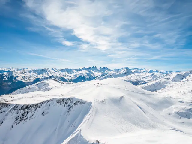 Paysage de montagnes enneigées avec des glaciers et des sommets sous un ciel bleu partiellement nuageux
