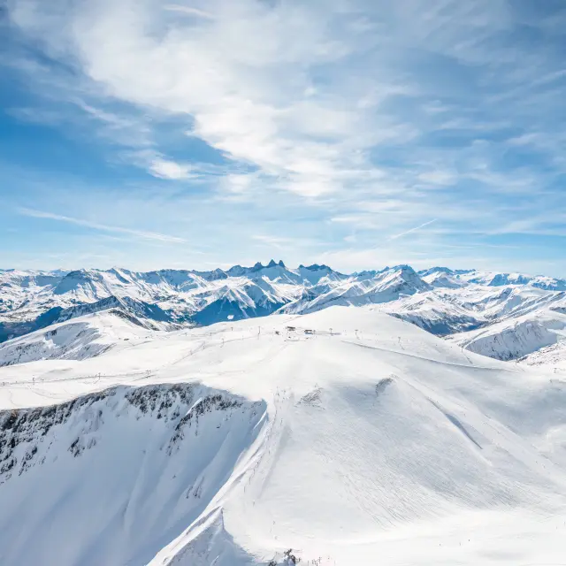 Paysage de montagnes enneigées avec des glaciers et des sommets sous un ciel bleu partiellement nuageux