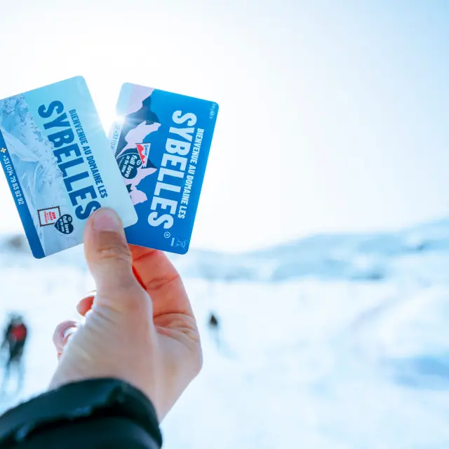 Deux forfaits de ski tenus dans une main avec un fond flou
