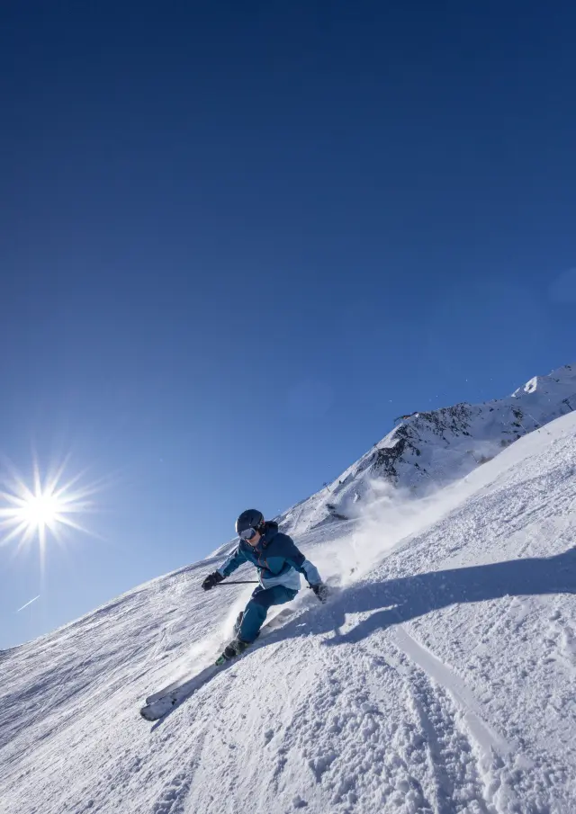 Skieur en tenue bleue descendant une pente enneigée sous un ciel dégagé