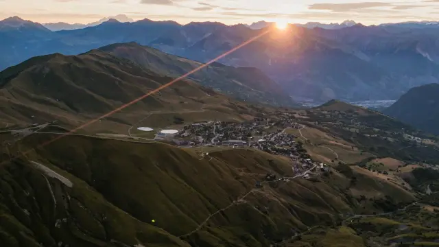 Village niché entre des montagnes au lever du soleil, avec des toits et une route sinueuse