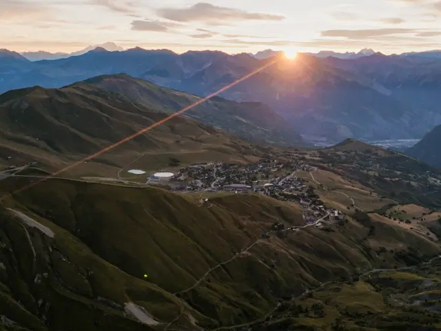 Village niché entre des montagnes au lever du soleil, avec des toits et une route sinueuse