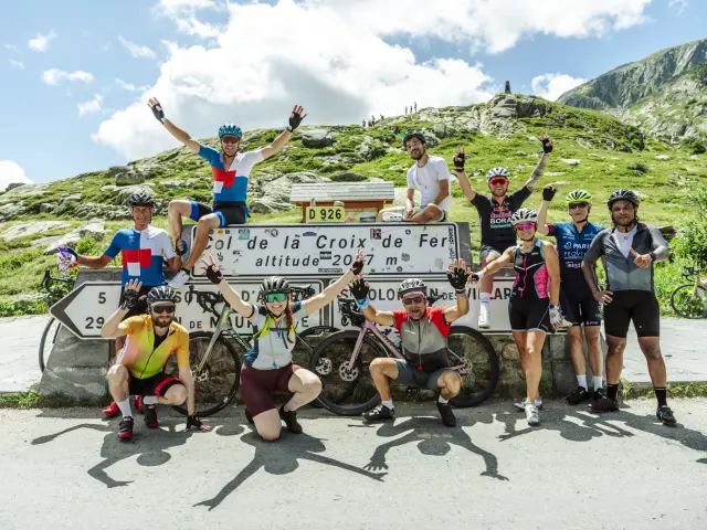 Cyclistes en compétition sur une route de montagne à La Croix de Fer, avec un panneau indiquant l'altitude de 2047 mètres