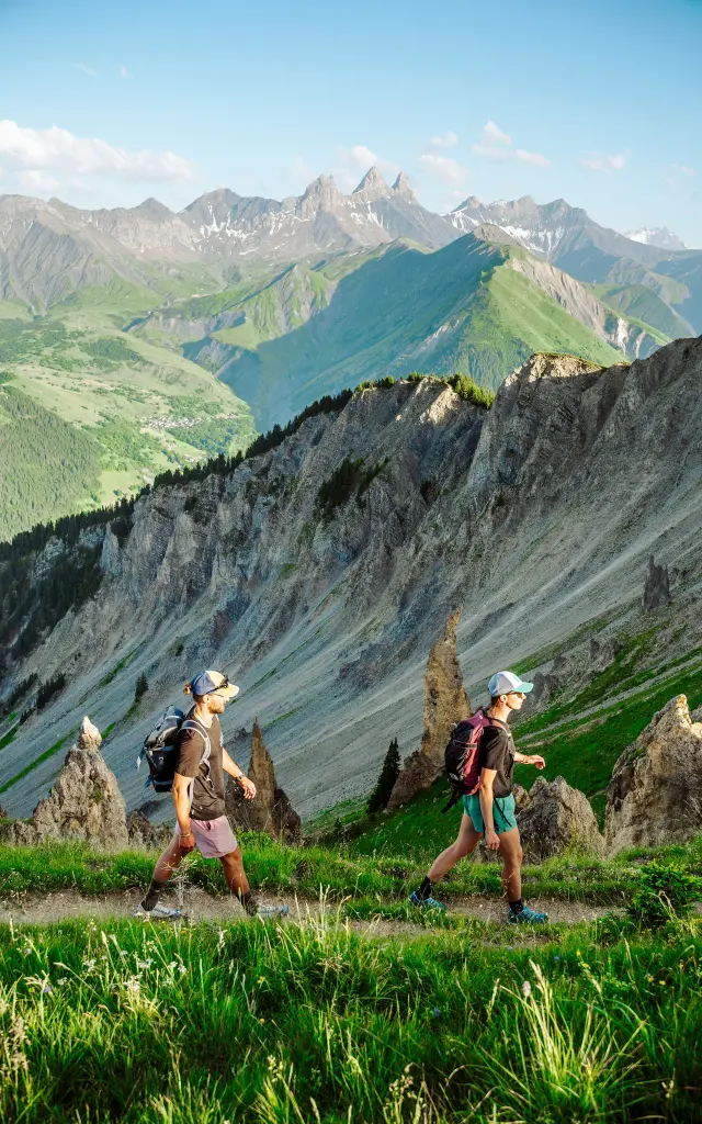 Deux randonneurs en tenue sportive marchant sur un sentier de montagne avec des sommets enneigés en arrière-plan