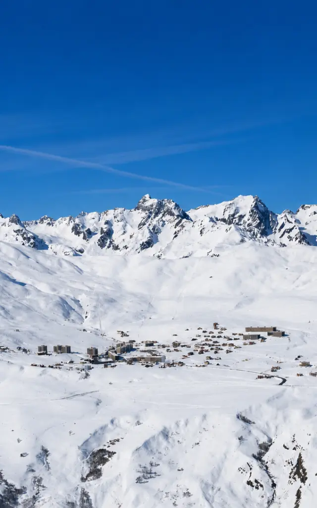 Vue d'un village de montagne enneigé avec des sommets enneigés en arrière-plan sous un ciel bleu dégagé