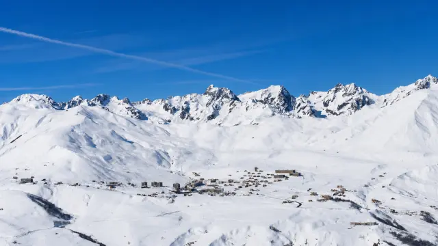 Vue d'un village de montagne enneigé avec des sommets enneigés en arrière-plan sous un ciel bleu dégagé