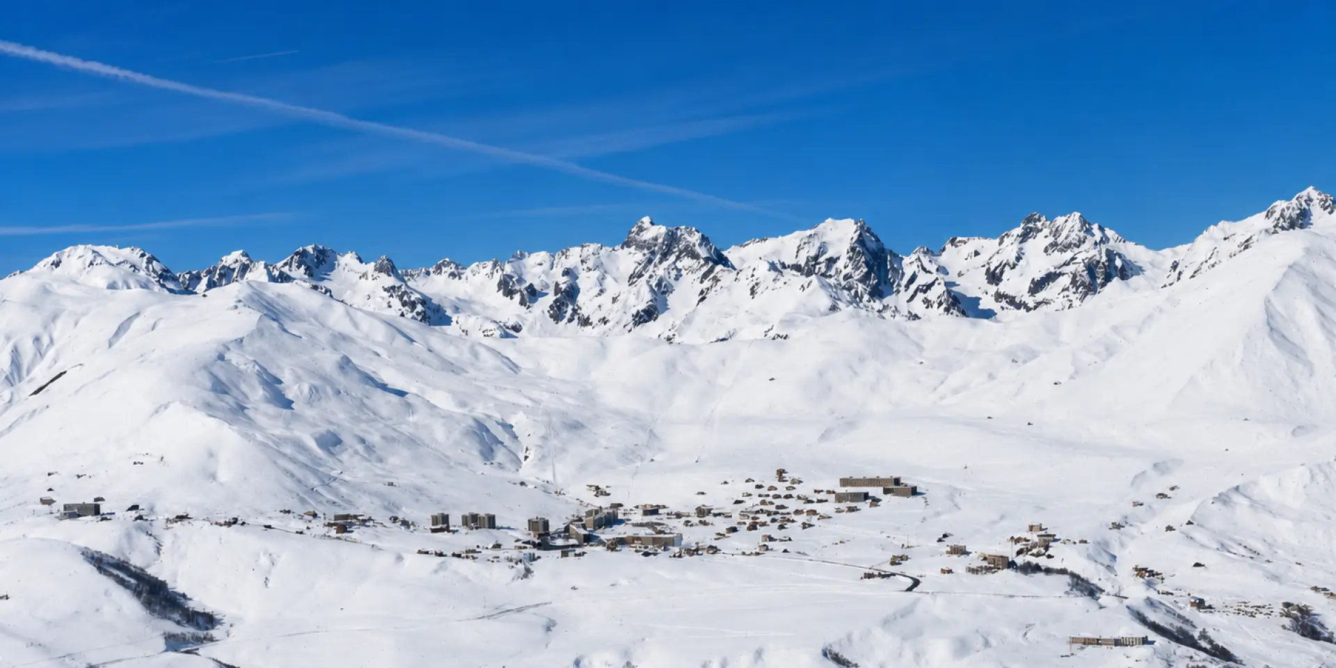Vue d'un village de montagne enneigé avec des sommets enneigés en arrière-plan sous un ciel bleu dégagé