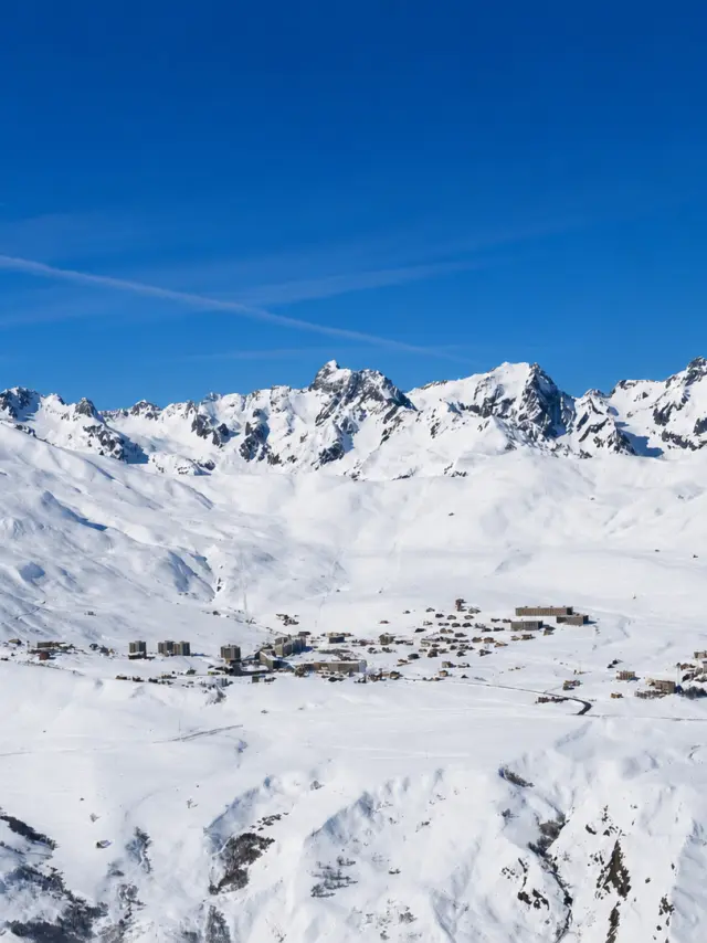 Vue d'un village de montagne enneigé avec des sommets enneigés en arrière-plan sous un ciel bleu dégagé