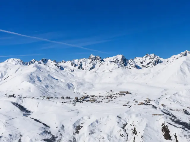 Vue d'un village de montagne enneigé avec des sommets enneigés en arrière-plan sous un ciel bleu dégagé