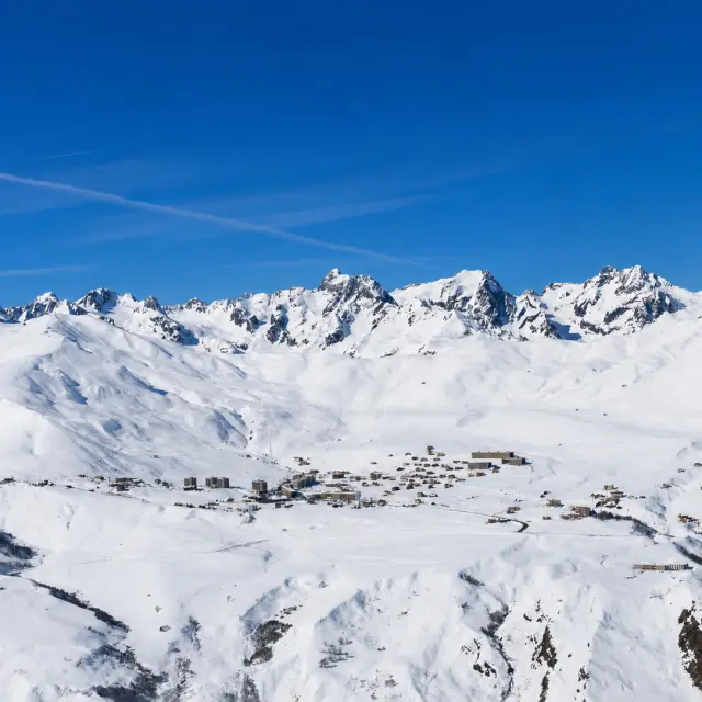 Vue d'un village de montagne enneigé avec des sommets enneigés en arrière-plan sous un ciel bleu dégagé