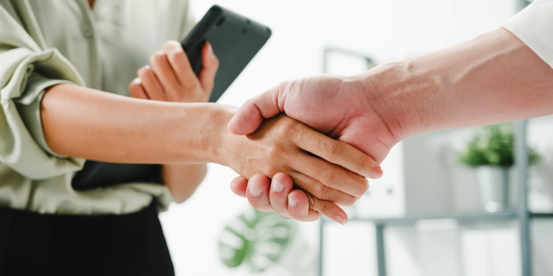 Multiracial group of young creative people in smart casual wear discussing business shaking hands together and smiling while standing in modern office. Partner cooperation, coworker teamwork concept.