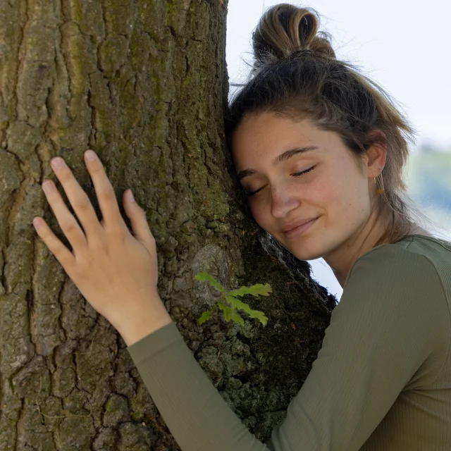 Contented young woman hugging a large tree with a blissful expression and her eyes closed in a concept of save the forest, stop deforestation, earth's day, connecting with nature and nature conservation. High quality photo
