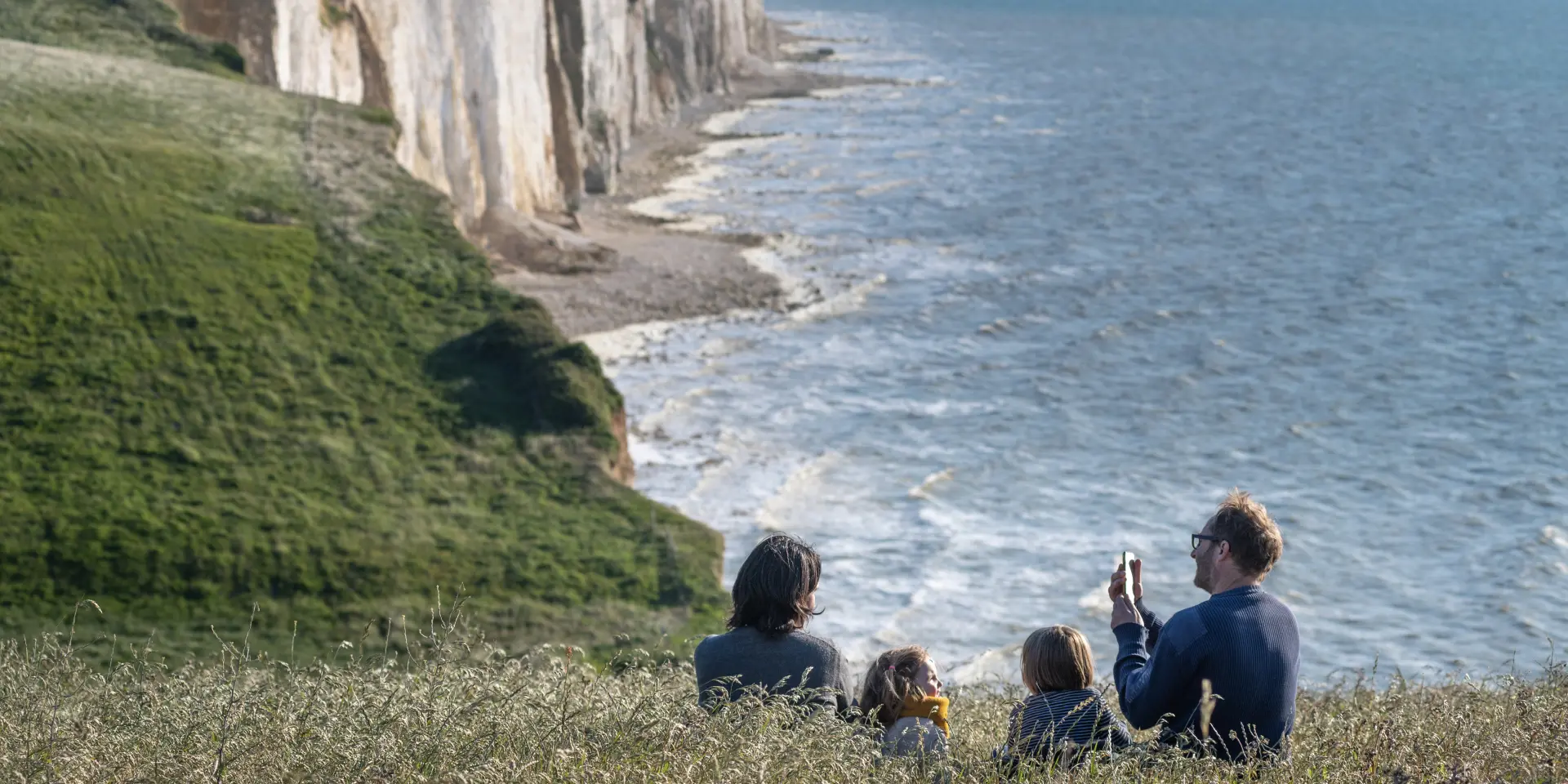 Une famille profitant du panorama sur le sentier du littoral pour faire une pause dans les champs