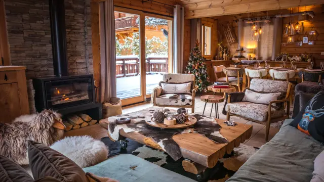 Interieur van een houten chalet met brandende open haard, warme inrichting en uitzicht op het besneeuwde landschap.