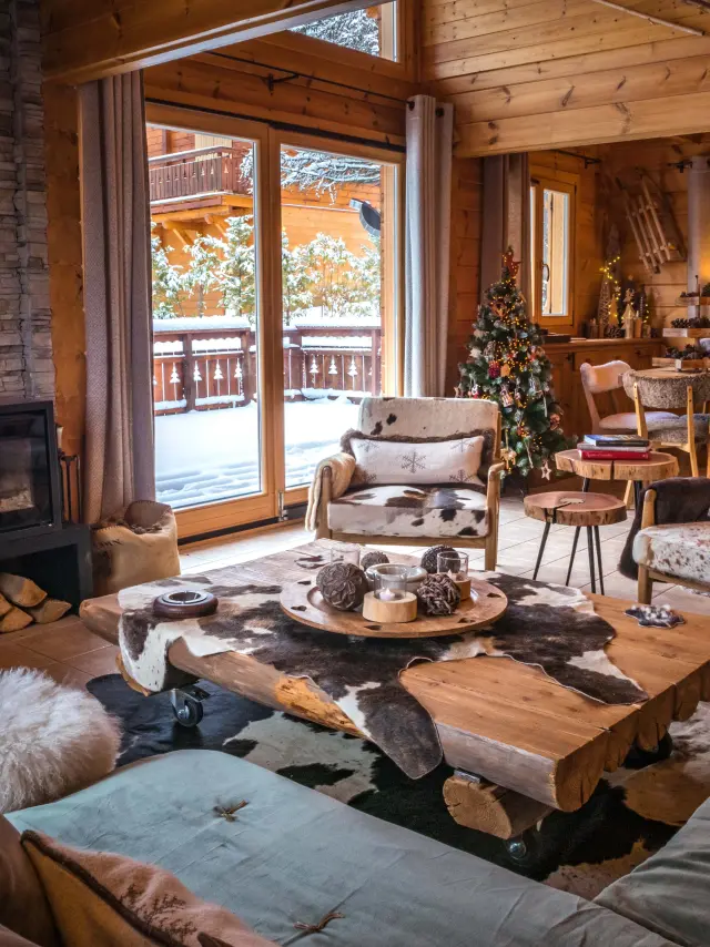 Intérieur d’un chalet en bois avec cheminée allumée, mobilier chaleureux et vue sur l’extérieur enneigé.