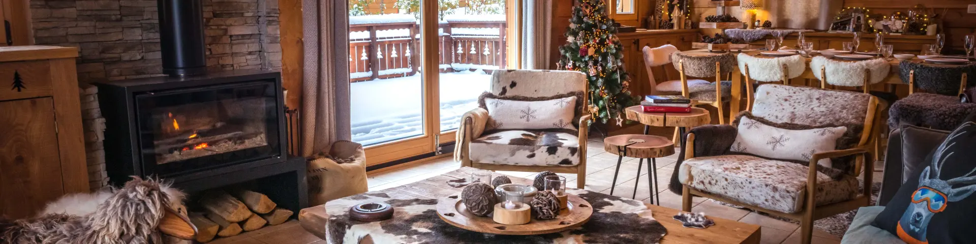 Interieur van een houten chalet met brandende open haard, warme inrichting en uitzicht op het besneeuwde landschap.