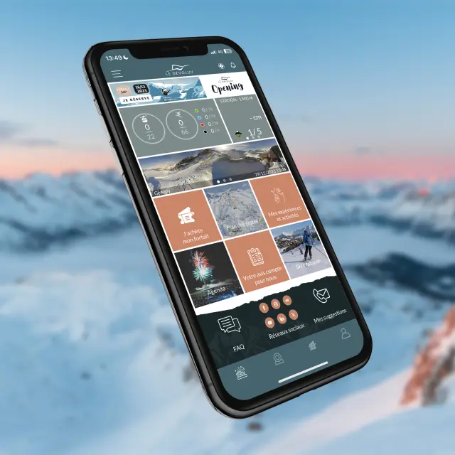 Smartphone affichant l’application mobile du Dévoluy avec des informations sur la station en arrière-plan montagneux enneigé.