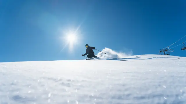 Skieur descendant une piste enneigée sous un grand soleil sur le domaine alpin du Dévoluy.