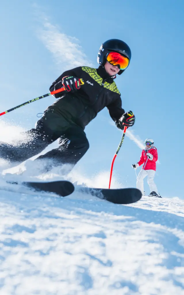 Quatre skieurs, dont des enfants, descendent une piste enneigée sous un ciel parfaitement bleu.