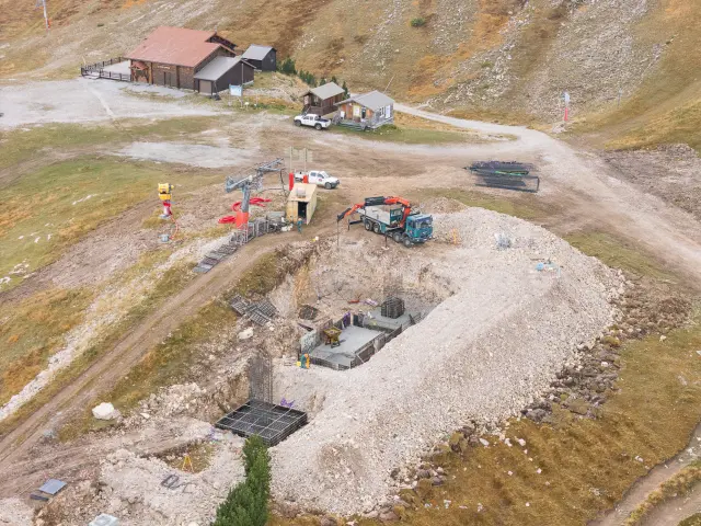 Vue aérienne d’un chantier en montagne avec excavation, ferraillage et dalle béton pour la future gare du télécabine.