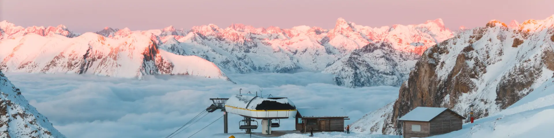 Sommet du domaine skiable du Dévoluy au Sommarel, avec une remontée mécanique entourée de neige et une mer de nuages face aux sommets alpins au lever du jour.