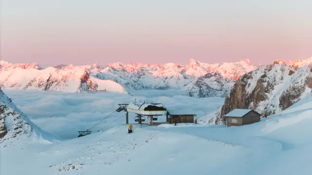 Top van het skigebied Dévoluy in Sommarel, met een skilift omgeven door sneeuw en een zee van wolken tegenover de bergtoppen bij zonsopgang.