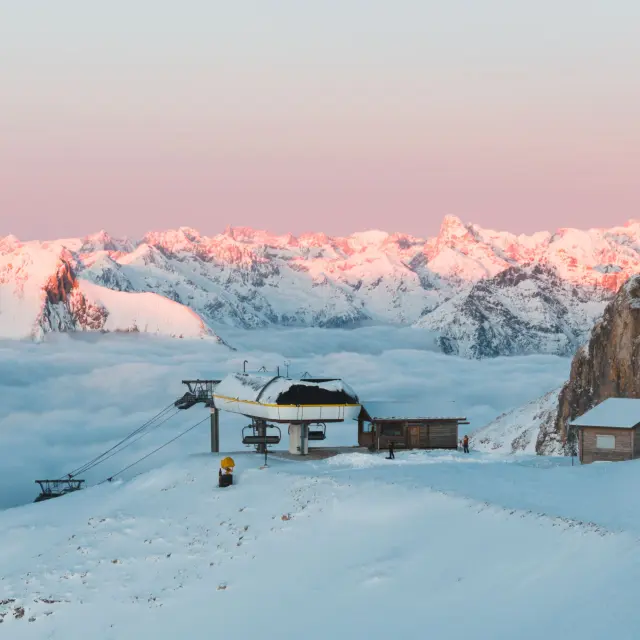 Sommet du domaine skiable du Dévoluy au Sommarel, avec une remontée mécanique entourée de neige et une mer de nuages face aux sommets alpins au lever du jour.