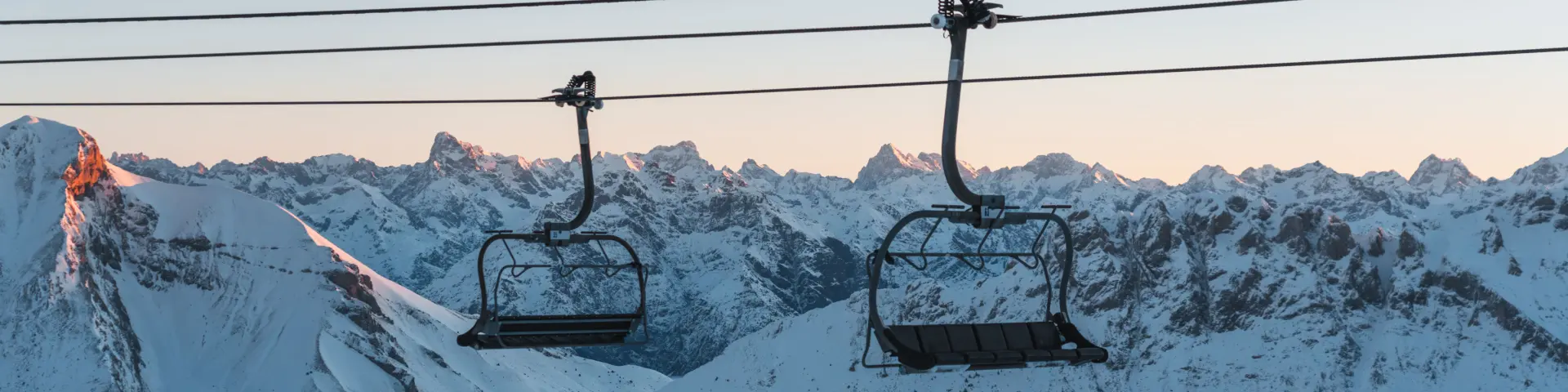 Two empty chairlifts above the snow-covered mountains of Dévoluy at sunrise.