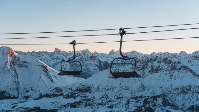 Deux télésièges vides au-dessus des montagnes enneigées du Dévoluy au lever du soleil.