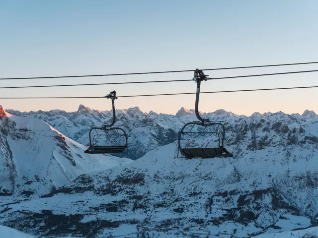 Twee lege stoeltjesliften boven de besneeuwde bergen van Le Dévoluy bij zonsopgang.