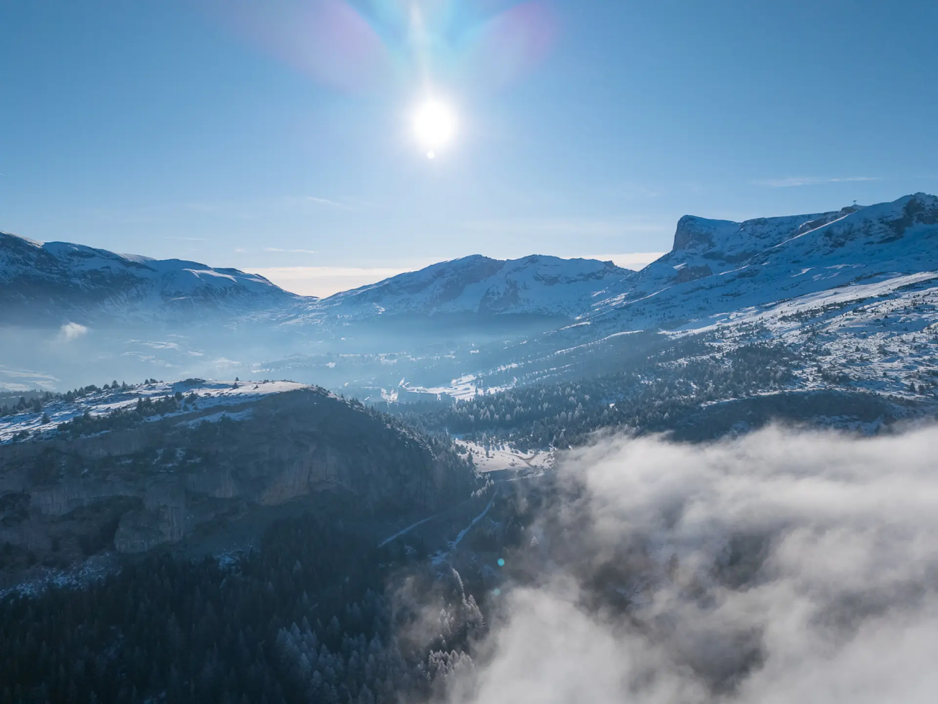 Winter landscape of Le Dévoluy with snow-covered mountains, misty valley and bright sun in the sky.