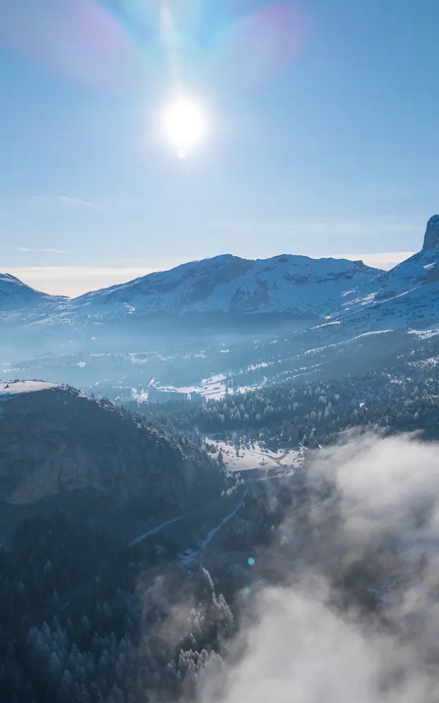 Winterlandschap van Le Dévoluy met besneeuwde bergen, een mistige vallei en een stralende zon.