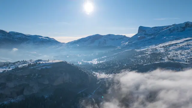 Paysage hivernal du Dévoluy avec montagnes enneigées, vallée embrumée et soleil haut dans le ciel.