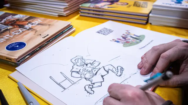 An illustrator drawing a comic strip at a table, surrounded by comic books during the Les Givrés de la BD event.