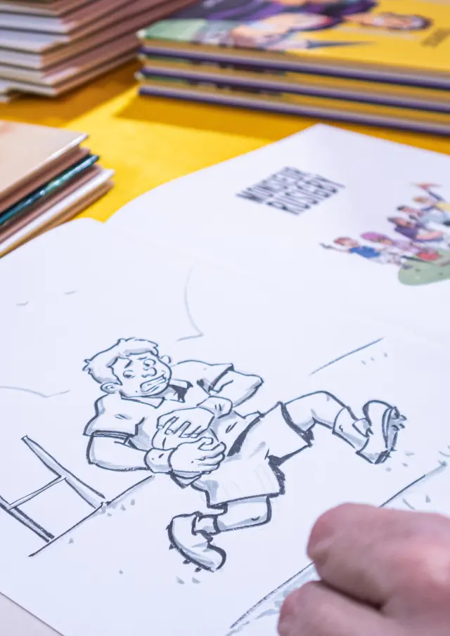 An illustrator drawing a comic strip at a table, surrounded by comic books during the Les Givrés de la BD event.