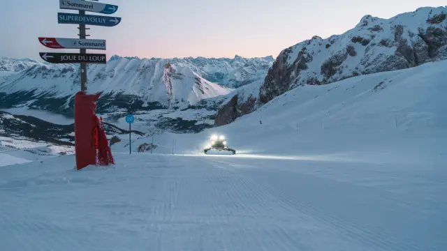 Snow groomer preparing a ski slope at dawn in the Le Dévoluy alpine ski area.