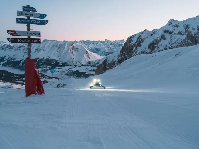 Pistenbully die bij zonsopgang een skipiste prepareert in het skigebied van Le Dévoluy.