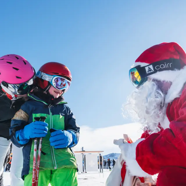 A child on skis meeting Santa Claus on the snowy slopes of Le Dévoluy with family.