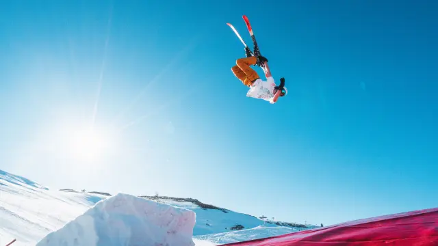 Skieur réalisant une figure acrobatique au-dessus d’un airbag sur le domaine skiable du Dévoluy, sous un ciel bleu et un soleil éclatant.