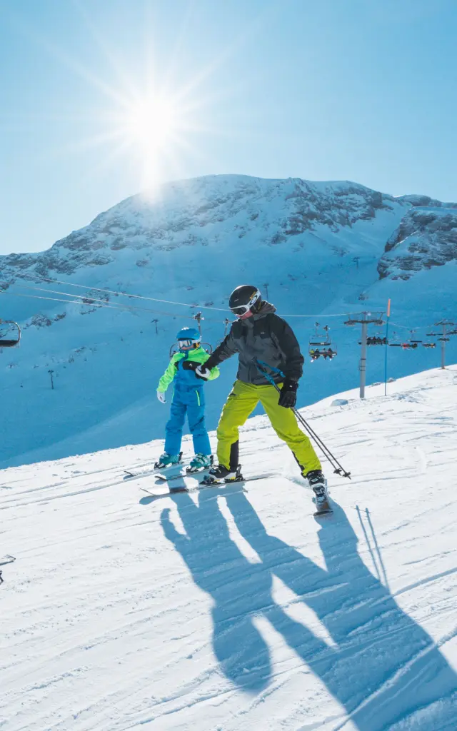 Gezin dat samen skiet op een zonnige piste in het alpineskigebied van Le Dévoluy met besneeuwde bergen op de achtergrond.
