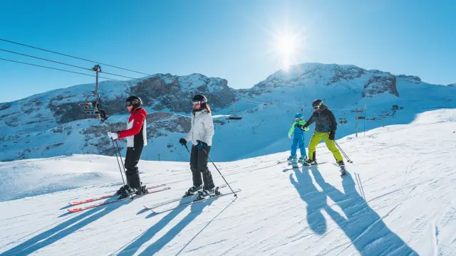 Gezin dat samen skiet op een zonnige piste in het alpineskigebied van Le Dévoluy met besneeuwde bergen op de achtergrond.