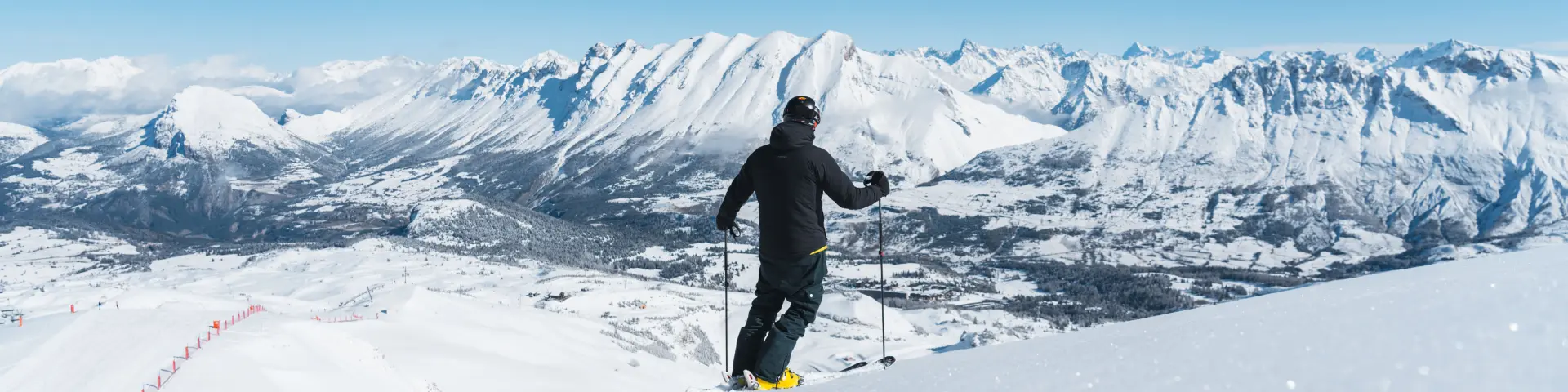 Skieur observant le paysage enneigé du massif du Dévoluy depuis une piste du domaine skiable.