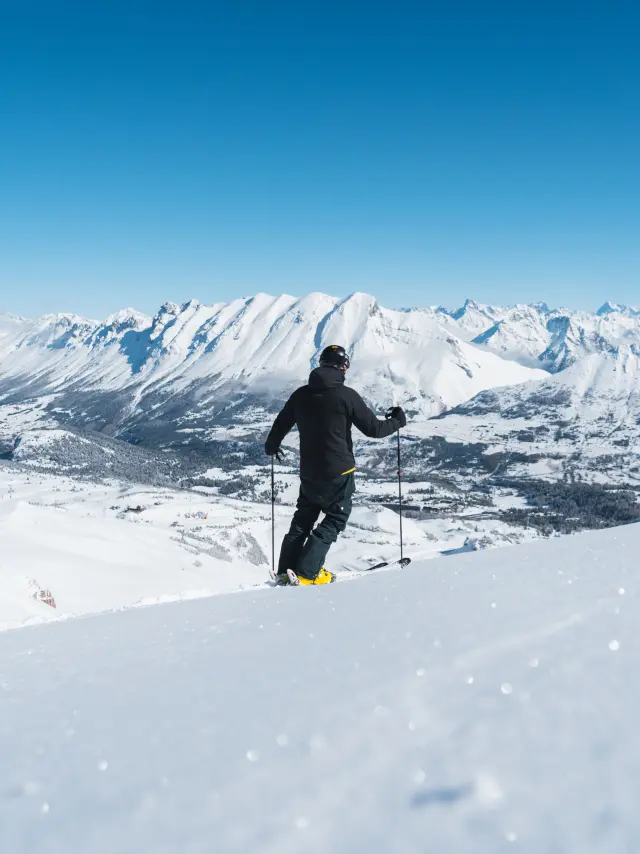 Skieur observant le paysage enneigé du massif du Dévoluy depuis une piste du domaine skiable.