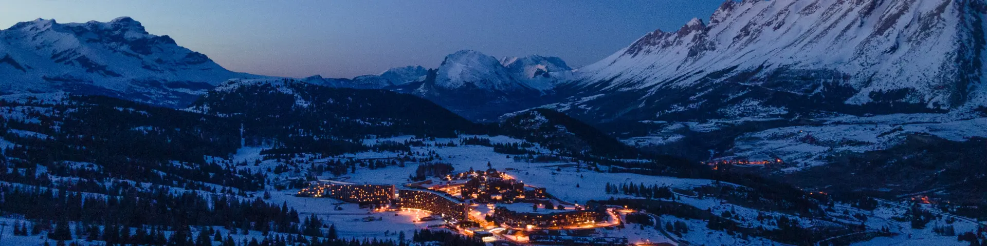 Aerial view of Superdévoluy resort illuminated at night and surrounded by snowy mountains.