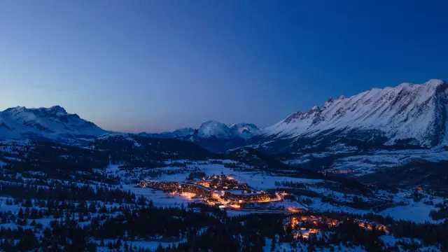 Vue aérienne de la station de Superdévoluy éclairée la nuit, entourée de montagnes enneigées.