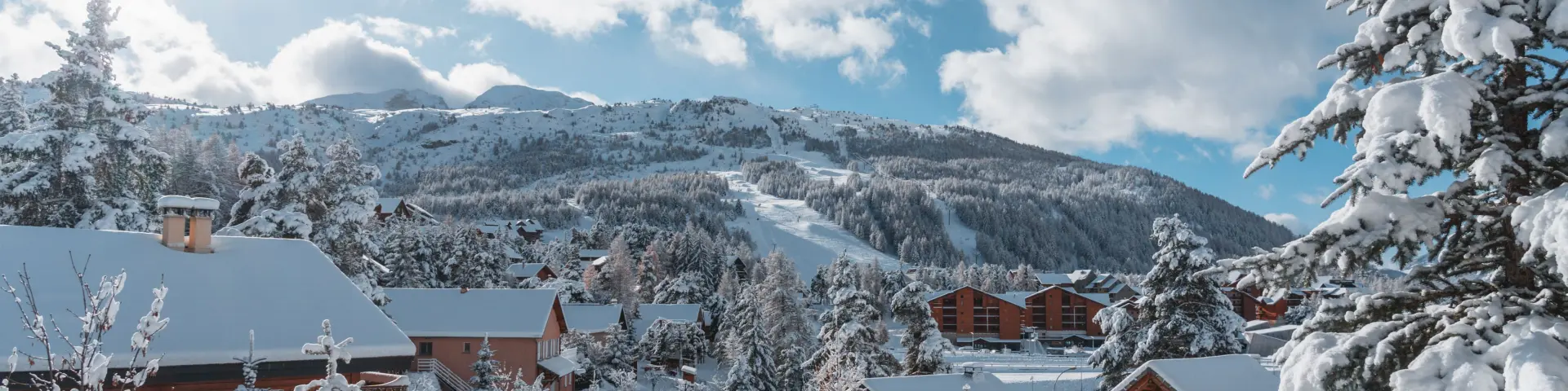 Wooden chalets surrounded by snow-covered trees in La Joue du Loup with ski slopes in the background.
