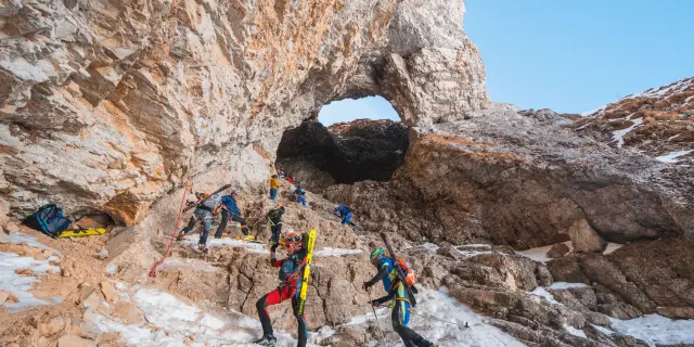 Ski-alpinisten lopen door een besneeuwde rotsdoorgang onder een natuurlijke rotsboog.